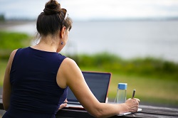 Image of a woman sitting outside making notes from her laptop