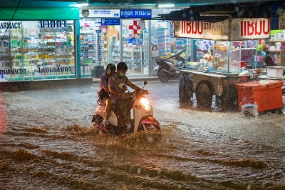 Two people riding a motor scooter through a flooded shopping area