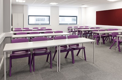 Image of an empty classroom with rows of tables and chairs 