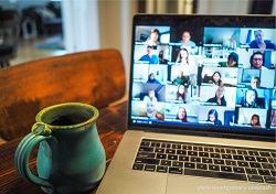 Image of a mug standing next to a laptop. The laptop is showing that a large online meeting taking place