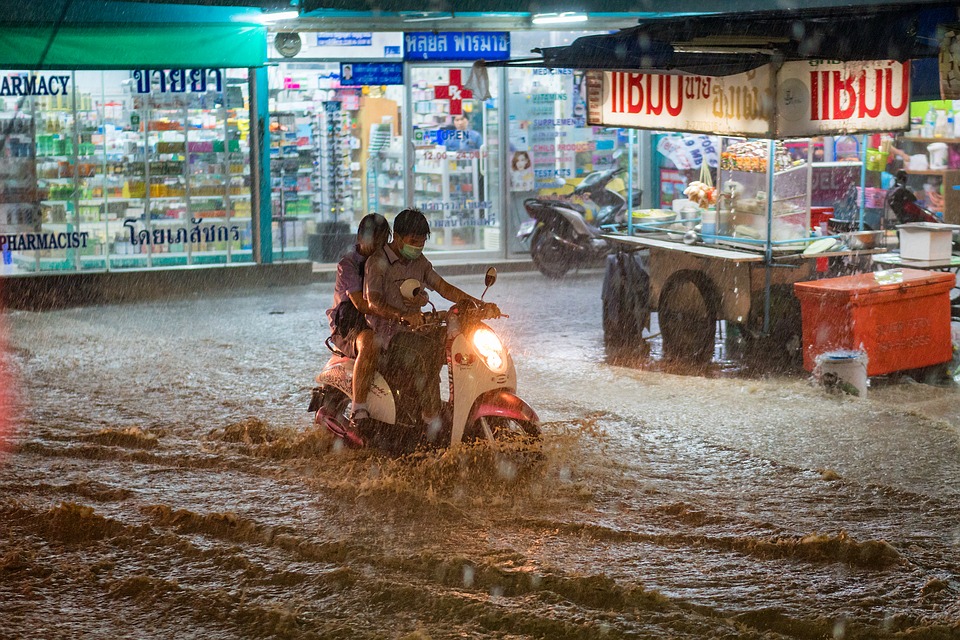 Two people drive through heavy flooding on a moped