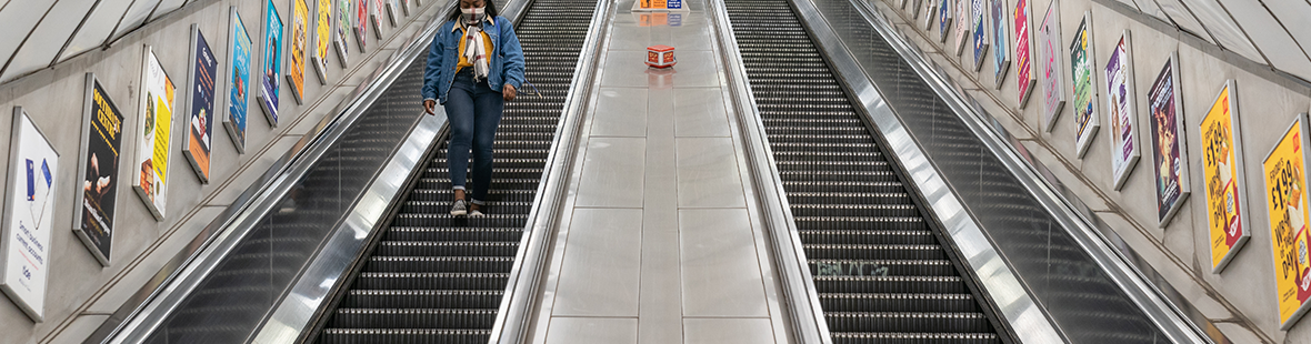 person wearing mask walking down empty escalator