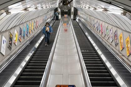 Person walking down a london tube escalator wearing mask