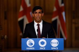 Rishi Sunak stands behind a podium with the words "Hands Face Space"