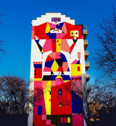 Mural of lady in bright primary colours on large building.